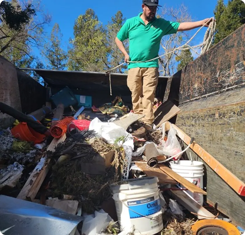 A man stands triumphantly on a large pile of garbage