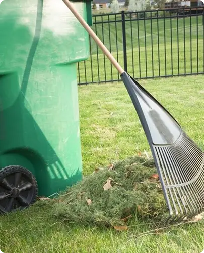 A green trash can beside a rake