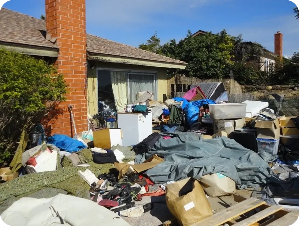 A cluttered pile of junk sits outside a house featuring a brick fireplace