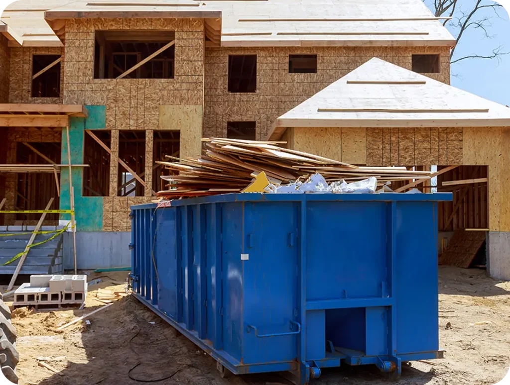 A dumpster placed in front of a house that is currently under construction