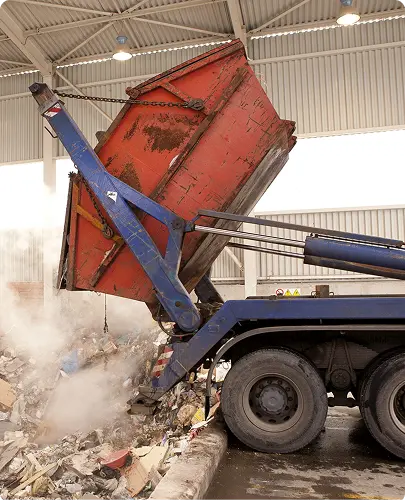A dump truck unloading a large pile of garbage onto the ground at a waste disposal site