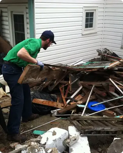 A man wearing a green shirt is actively working on a large pile of debris